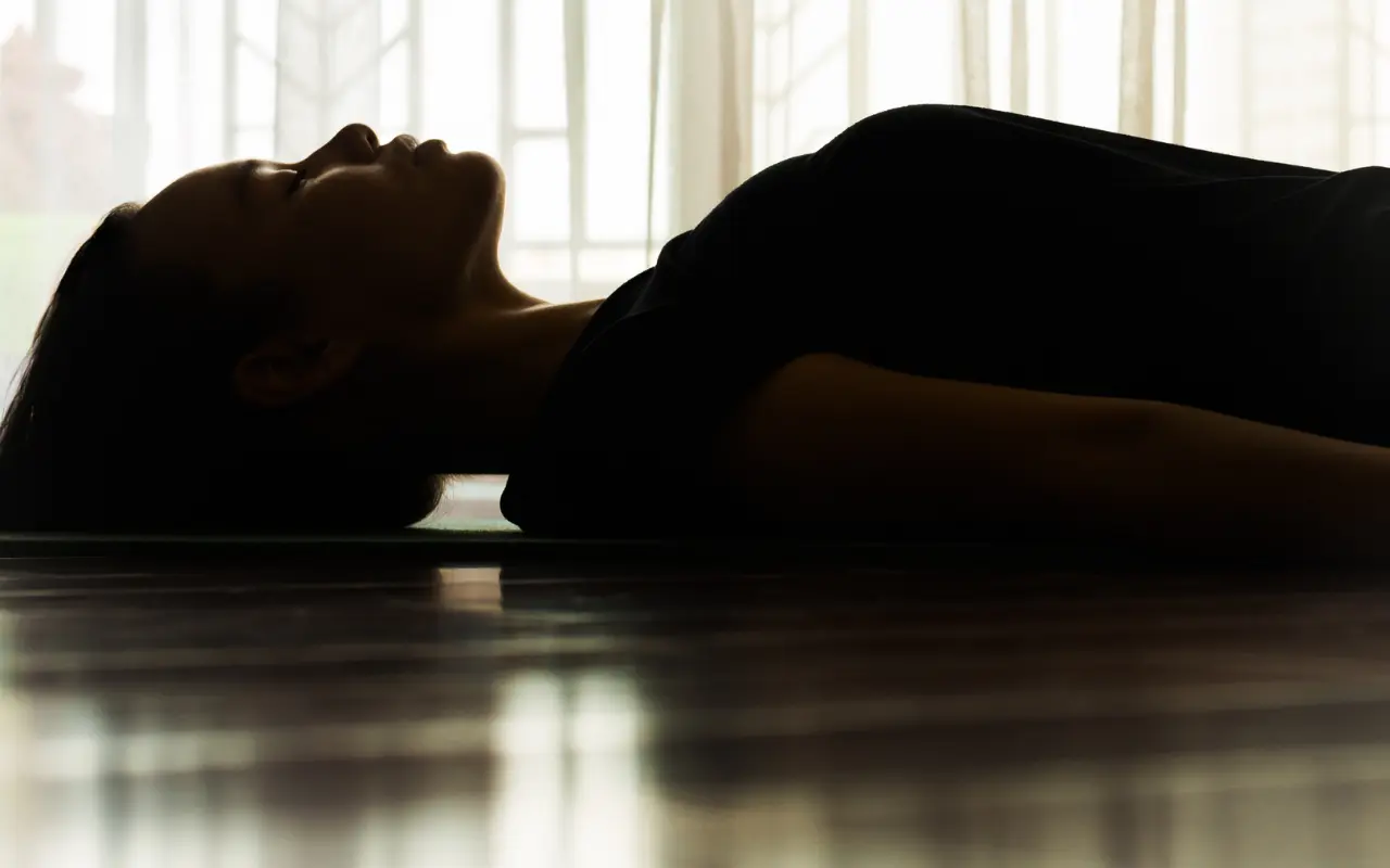 A serene moment of stillness and self-reflection, as a woman lies peacefully on the floor, bathed in soft light from a nearby window
